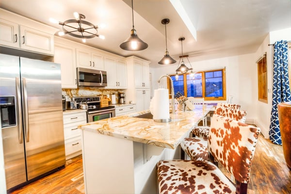Modern kitchen with white cabinetry, marble countertops, stainless steel appliances, and pendant lighting overlooking open-plan living area with city views.